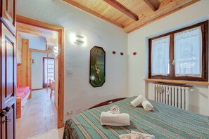 A bedroom with a bed, a window with curtains, a radiator, and a door leading to another room. - Appartamento Rochebrune 200m From Ski (Claviere)