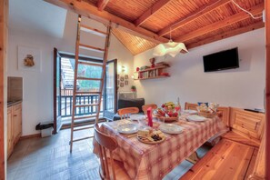A dining area with a wooden table set for four, a ladder, and a television mounted on the wall. - Appartamento Rochebrune 200m From Ski (Claviere)