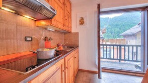 Una cocina con armarios de madera, una estufa y vistas a un balcón con montañas al fondo.