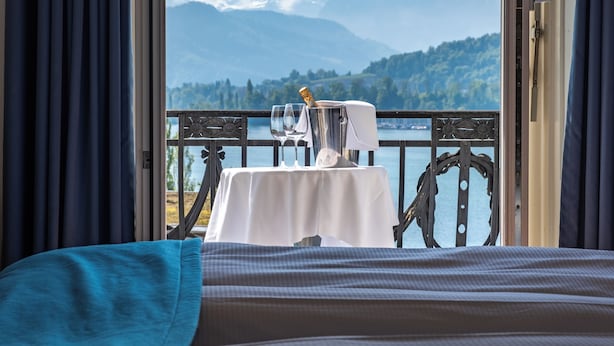 A balcony with a table set for two, overlooking a lake and mountains.