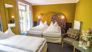 Habitación de hotel con dos camas, una silla, una mesita con un florero y un espejo.