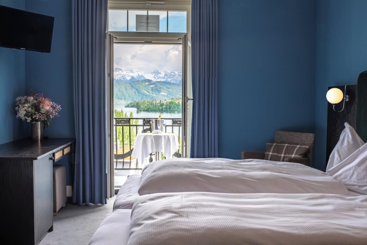 A hotel room with a large bed, a desk with a vase of flowers, and a balcony with a table and chairs.