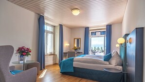A modern hotel room with a large bed, a seating area with a table, and a view of the outdoors.