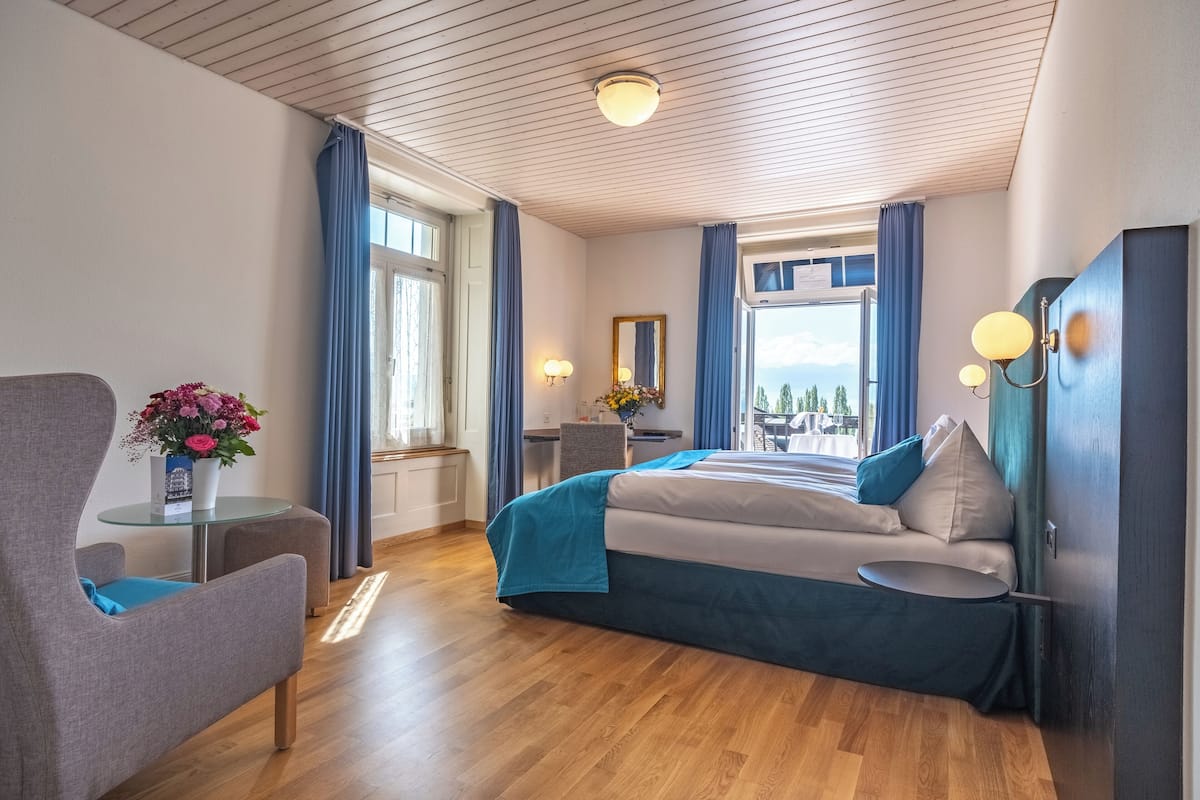 A modern hotel room with a large bed, a seating area with a table, and a view of the outdoors.