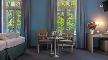 Habitación de hotel con cama, dos sillones, una mesita, un escritorio y un ventanal con cortinas.