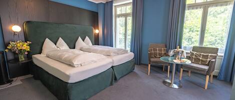 A hotel room with a large bed, a small table with a glass top, a chair, and a window with curtains.