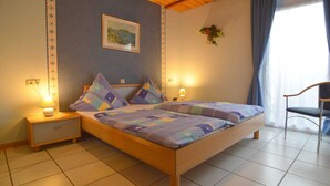 A bedroom with a wooden bed, two bedside tables with lamps, a framed picture on the wall, and a window with curtains.