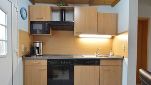 A compact kitchen with wooden cabinets, a microwave, a stove, and a dishwasher.
