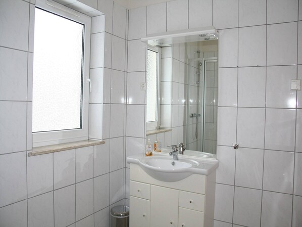 A bathroom with white tiles, a window, a sink with a mirror, and a shower. - Bungalow in Eifel near Forest and Mountains (Hinterhausen - Gerolstein)