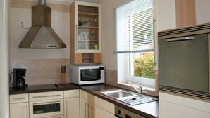 A modern kitchen with a built-in microwave, a coffee maker, and a window with blinds. - Bungalow near Eifel Ski Lift (Hinterhausen - Gerolstein)