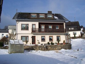 A two-story house with a balcony, a stone foundation, and a greenhouse in the foreground. - Ferienwohnung im Sauerland Hillside (Hallenberg-Hesborn)