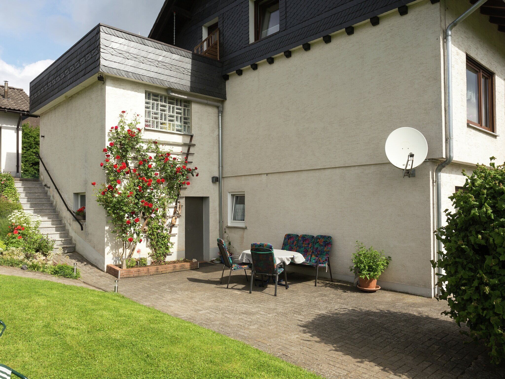 A residential building with a staircase leading to a balcony, a satellite dish, and outdoor seating area with chairs and a table.