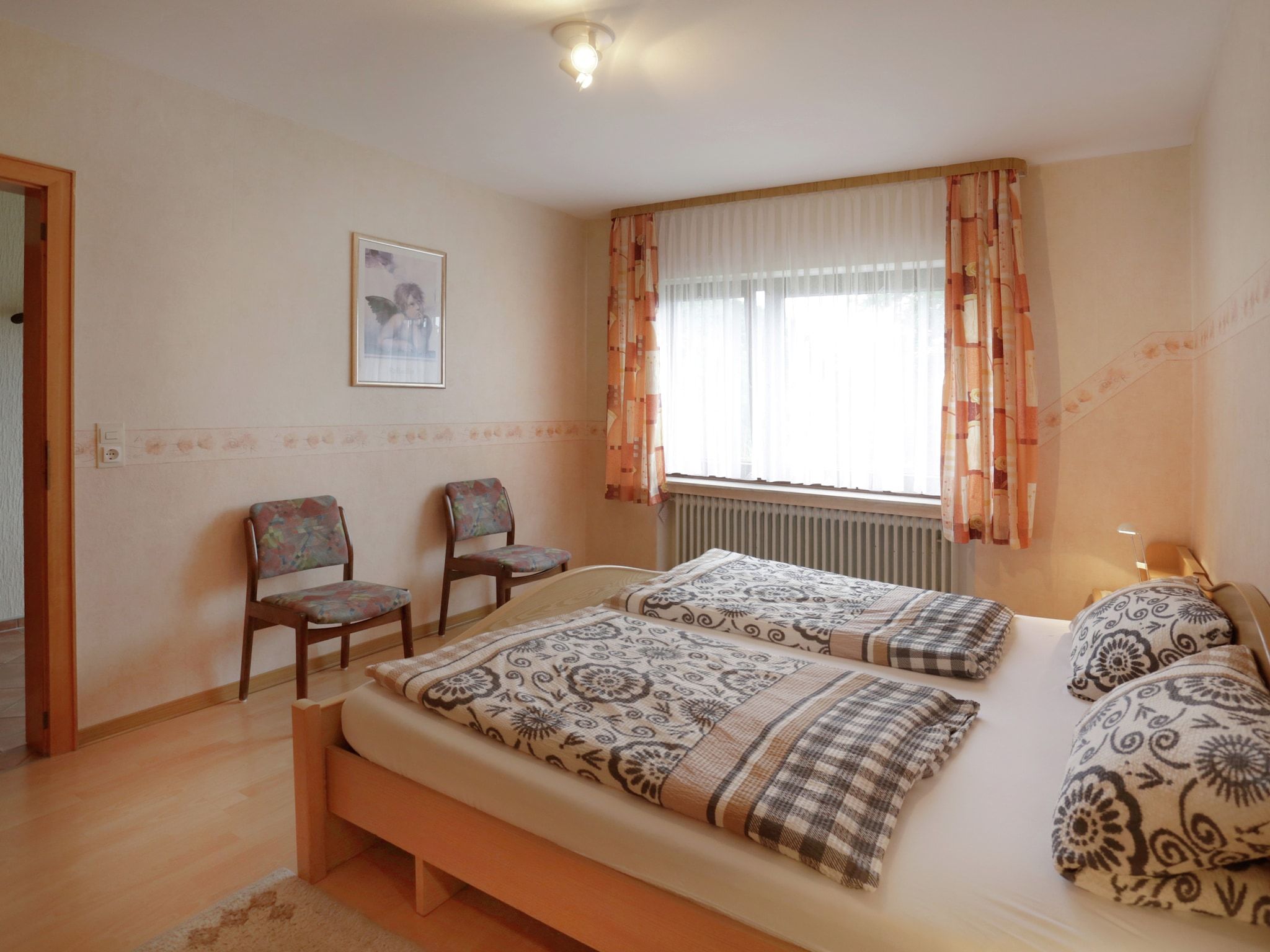 Un dormitorio con dos camas, una ventana con cortinas, un radiador y dos sillas.