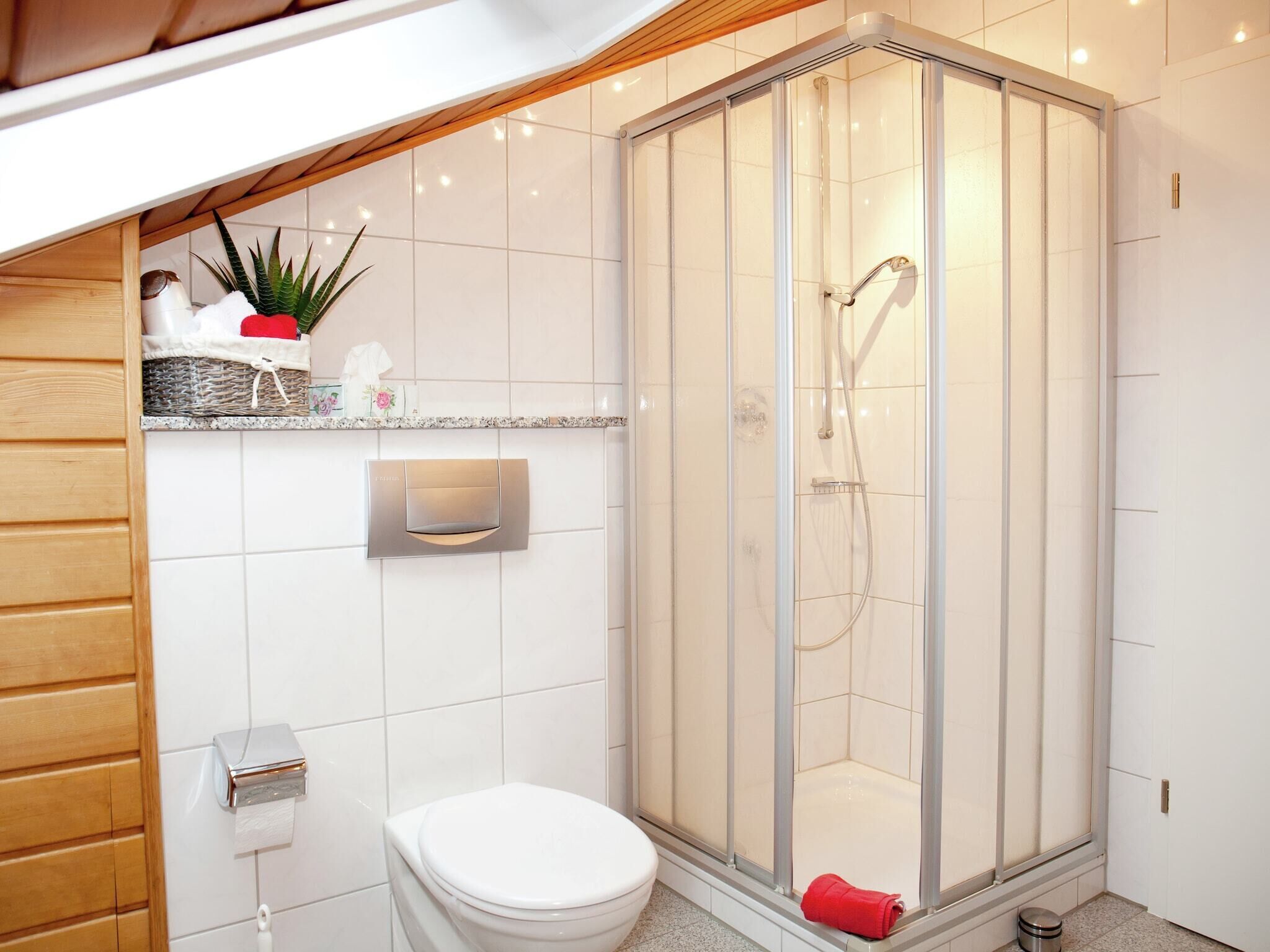 Et moderne badeværelse med en glasvægs-brusekabine, toilet og en hylde med toiletartikler.