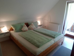 Une chambre à coucher avec un lit en bois, des coussins verts, une table de chevet avec une lampe et une fenêtre avec des rideaux.