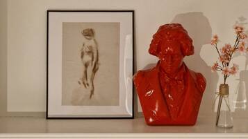A white shelf with a framed black and white photograph, a red sculpture, and a small vase with flowers.