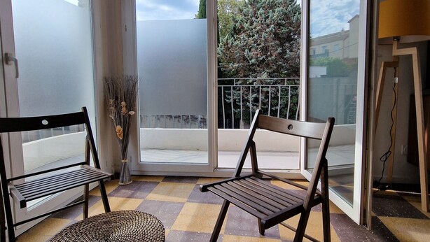 A balcony with two wooden chairs, a wicker stool, and a glass door leading outside.
