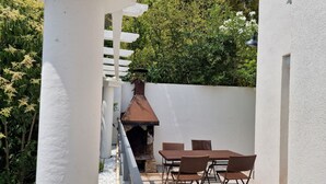 A patio with a white pergola, a brick oven, and a table with chairs.