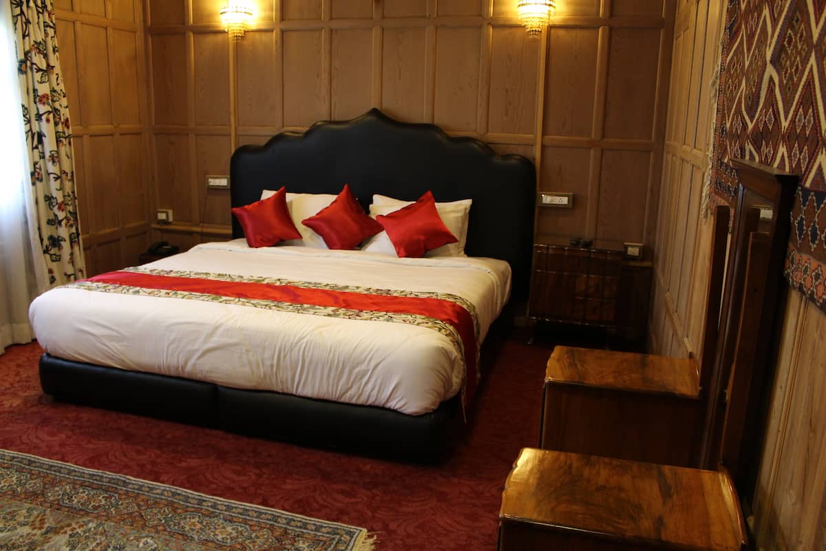A large bed with a dark headboard, red and white pillows, and a red and white bedspread. There is a wooden bench beside the bed and a patterned rug on the floor.