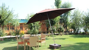 An outdoor seating area with a table and chairs, a large umbrella, and a lawn. - New York Houseboat (Srinagar)