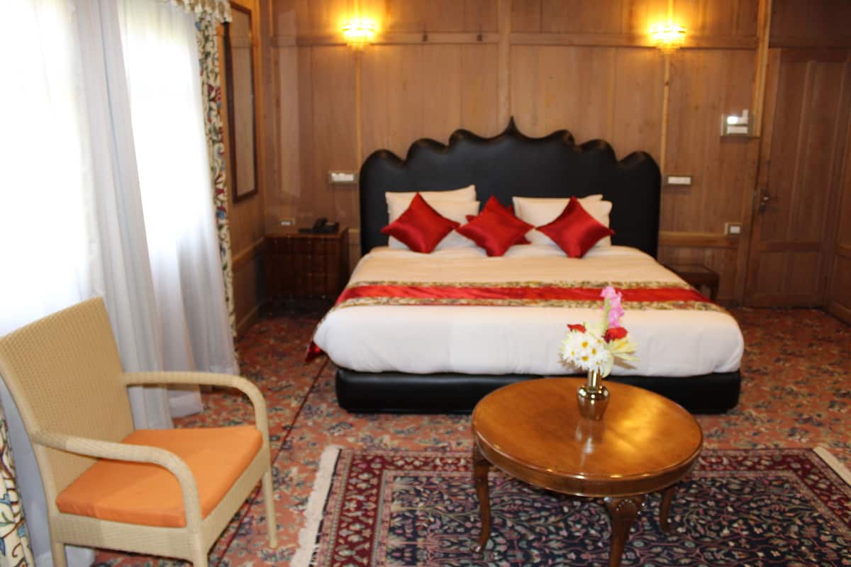 A hotel room with a large bed, a chair, a small table, and a decorative vase.
