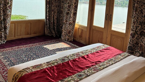 A room with a large bed, wooden ceiling, and a view of a lake. - New York Houseboat (Srinagar)