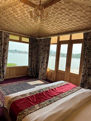 A room with a large bed, wooden ceiling, and a view of a lake. - New York Houseboat (Srinagar)