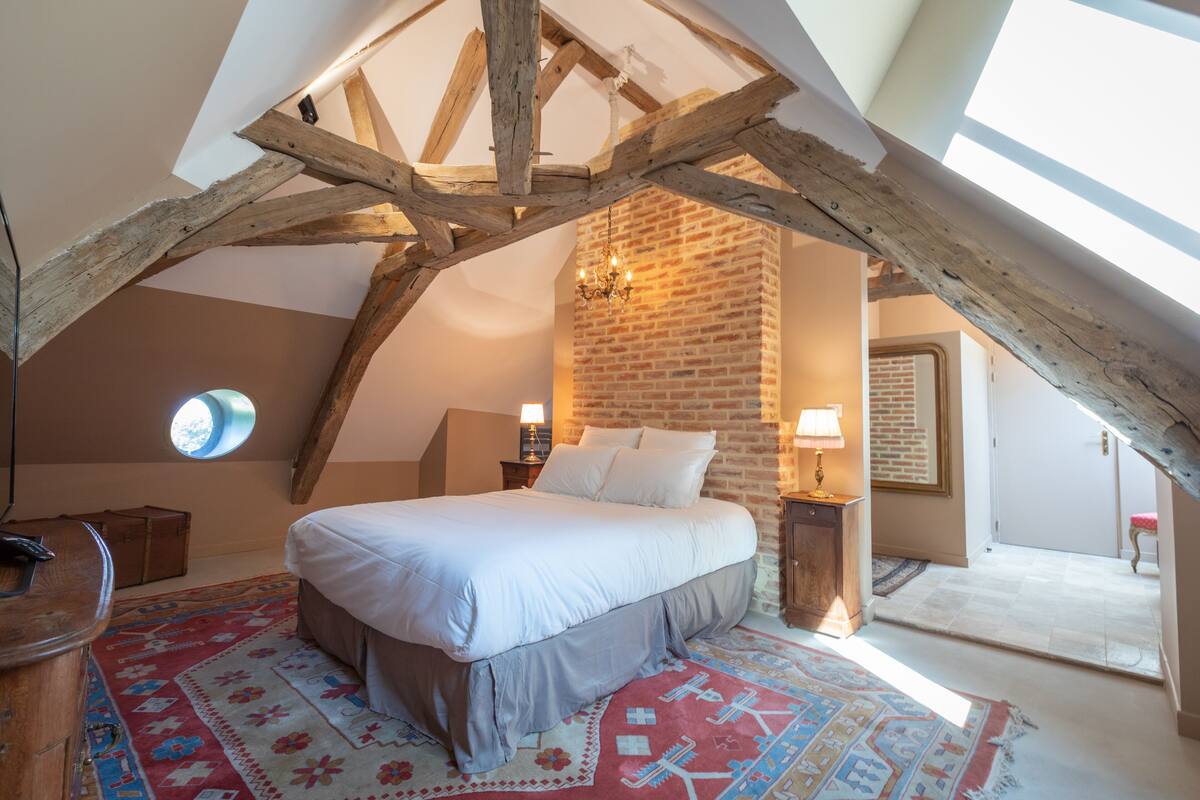 A bedroom with a large bed, a brick wall, a chandelier, and a skylight.