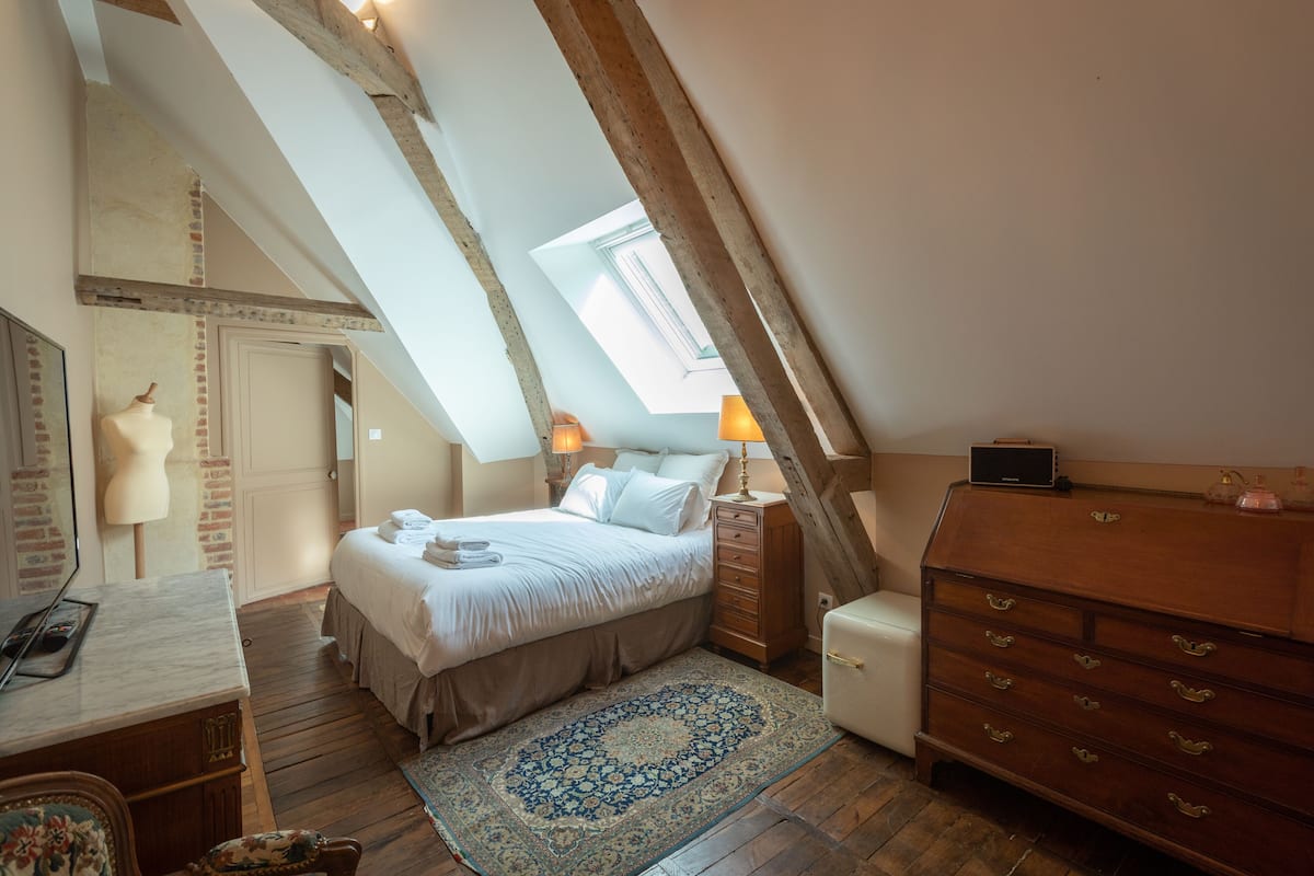 A bedroom with a sloped ceiling, a bed, a dresser, a desk, and a mirror.