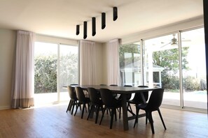 A dining area with a large table and chairs, large windows, and a ceiling fan.