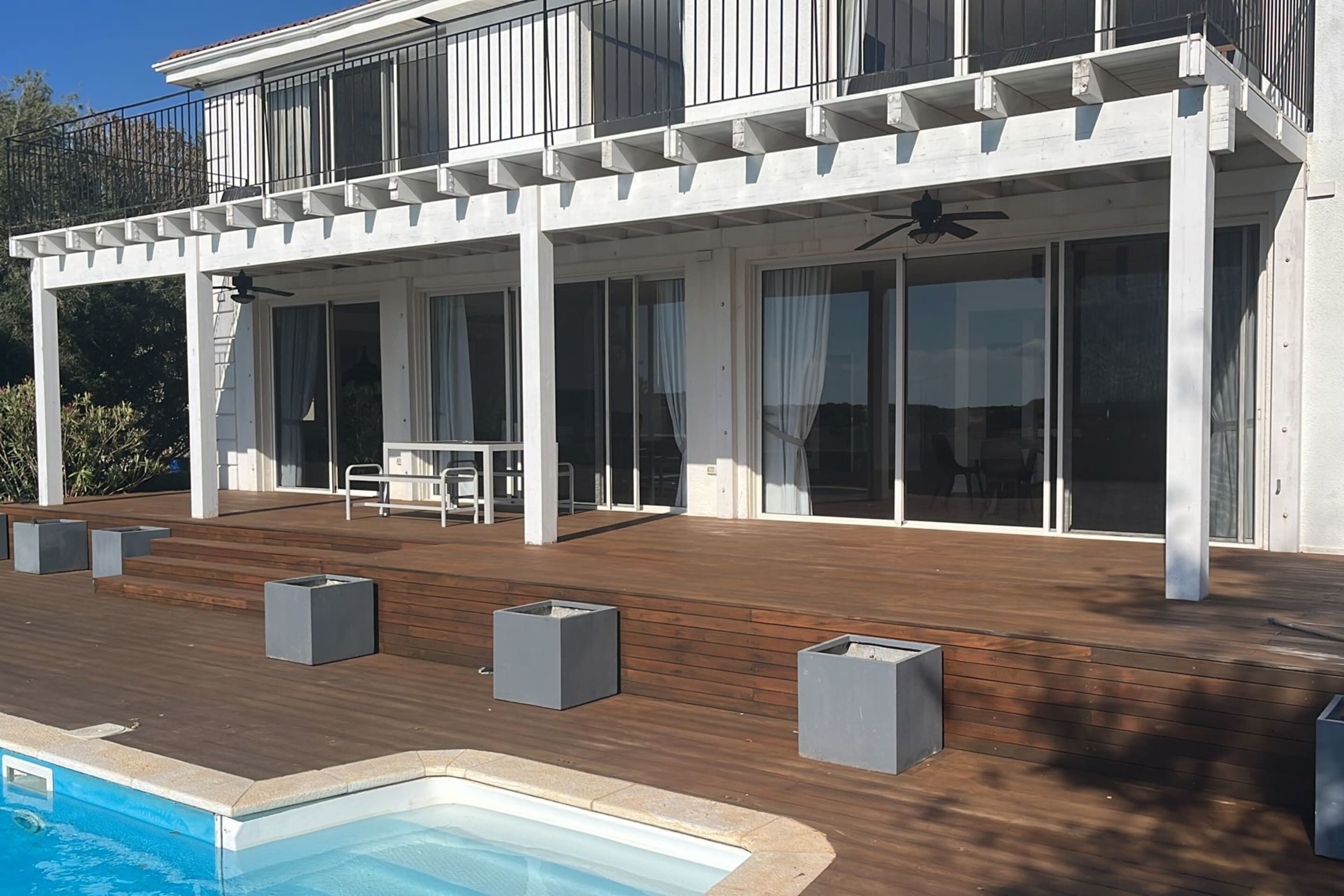 Ein modernes Haus mit einer Holzterrasse, einem Swimmingpool und einer Terrasse mit Sitzgelegenheiten.