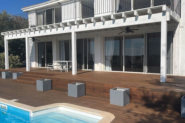 A modern house with a wooden deck, a swimming pool, and a patio with seating.