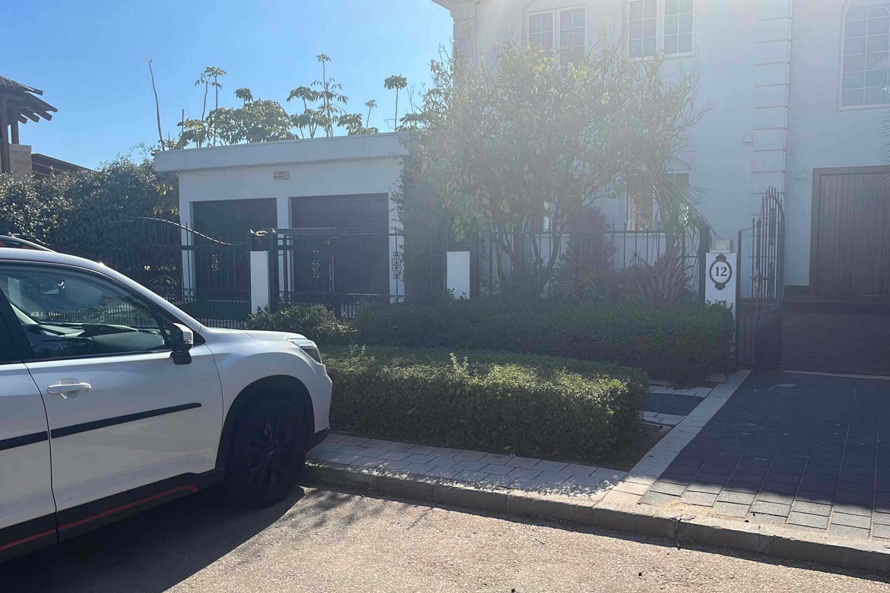 A white car parked on a paved road with a gated entrance and a building in the background.
