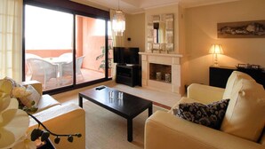 Una sala de estar con sofá, mesa de centro, televisor, chimenea y un balcón con mobiliario exterior.