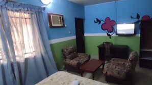 A room with a bed, two armchairs, a small table, a TV, and a wall with a floral design. - Townhall Hotel & Suites (Lagos)