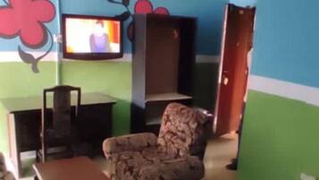 Una habitación con una cama, una silla, un televisor y una pared decorada con un diseño floral.