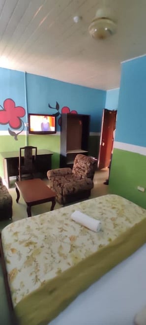 A room with a bed, a chair, a television, and a wall with a flower design. - Townhall Hotel & Suites (Lagos)