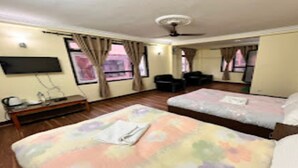 Habitación de hotel con dos camas, un televisor de pantalla plana montado en la pared, un ventilador de techo y una ventana con cortinas.