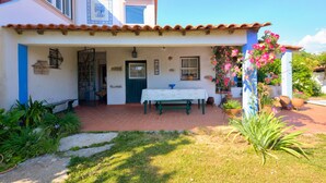Una casa de dos pisos con techo de tejas, un porche con banca y plantas en macetas.