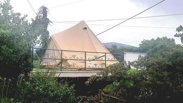 A tent-like structure with a metal railing, surrounded by dense foliage and trees.