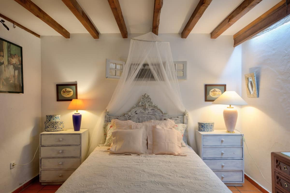 Ein Schlafzimmer mit einem Himmelsbett, zwei Nachttischen mit Lampen und einem Beistelltisch ebenfalls mit einer Lampe.
