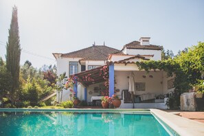 A poolside view of a house with a covered patio, potted plants, and a clear blue pool. - Adore Portugal Lousã (Lousa)