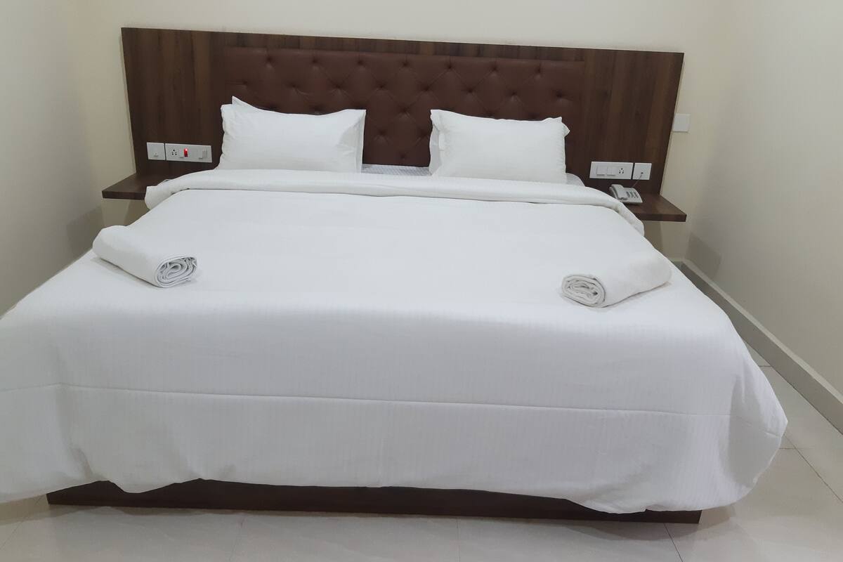 A neatly made bed with a tufted headboard, white bedding, and a small bedside table with a phone and a power outlet.