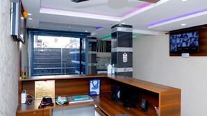 A modern reception desk with a wooden finish, a large flat-screen TV mounted on the wall, and a staircase leading to an upper level. - CNR Residency Madanapalle (Madanapalle)