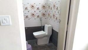 A small bathroom with a toilet, a shower, and a purple trash bin. - CNR Residency Madanapalle (Madanapalle)