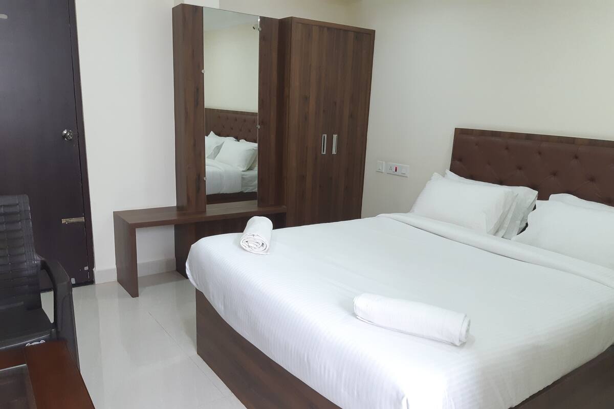 A neatly made bed with white linens, a wooden headboard, and a large mirror above it.