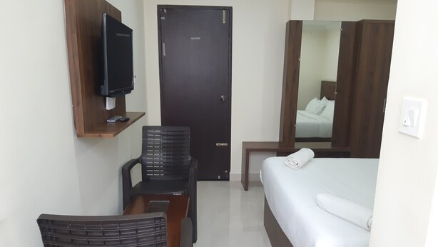 A hotel room with a bed, a desk with a chair, a television, and a wardrobe. - CNR Residency Madanapalle (Madanapalle)