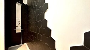 A bathroom with a black hexagonal tile wall, a white sink, and a shower area. - La Little House de Dinant – Esc’Appart (Dinant)