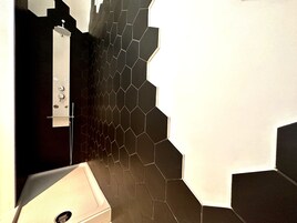 Un baño con pared de azulejos hexagonales negros, un lavamanos blanco y una zona de ducha.