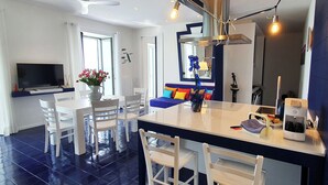A modern kitchen with a central island, white chairs, a dining table, and a TV. - In the blue painted blue (Campania)